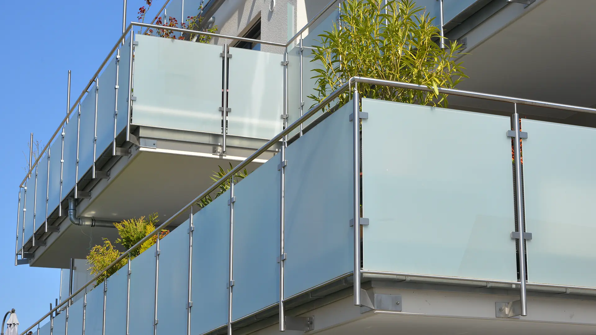 Balkon mit Edelstahl-Geländer und Sichtschutz aus Milchglasplatten an der Fassade eines modernen Mehrfamilien-Wohnhauses